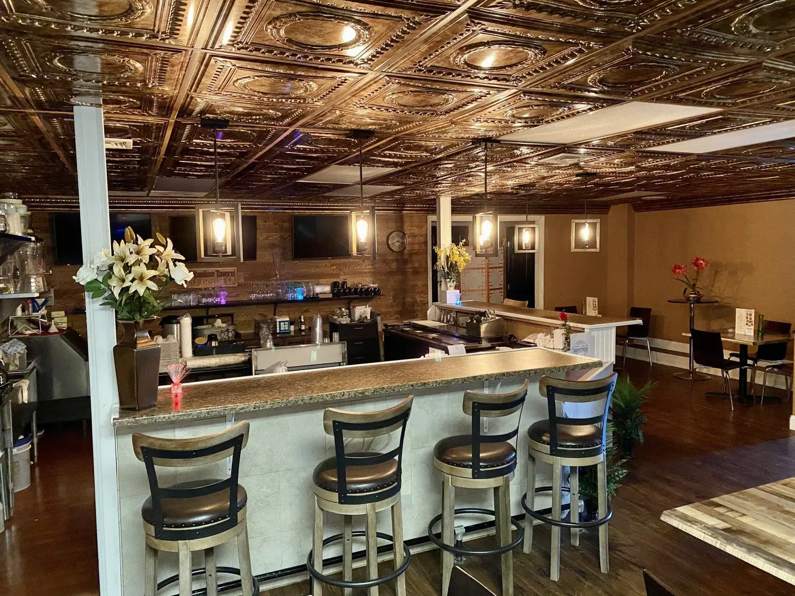 The Titanium Tavern bar — a granite bar top with leather-topped stools, pressed-tin ceiling, pendant lighting, and wall-mounted TVs
